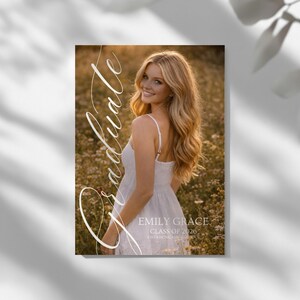 Peut inclure: Annonce de remise de dipl&ocirc;me avec une femme souriante en robe blanche dans un champ de fleurs. Le mot "Graduate" est &eacute;crit en script. L'annonce comprend le nom "Emily Grace" et "Class of 2026".
