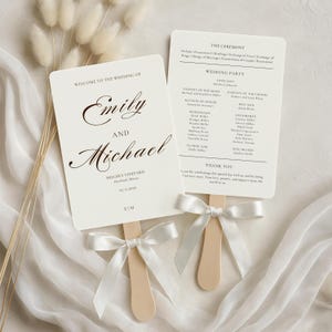 May include: Two ivory wedding fans with wooden handles and white satin ribbons. The fans display the names "Emily and Michael" and wedding details. One fan lists the ceremony details and wedding party.
