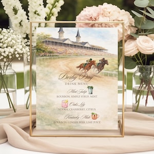 May include: A framed "Derby Day" drink menu with a watercolor illustration of a horse race. The menu lists three cocktails: Mint Julep, Oak's Lily, and Kentucky Mule. The frame is gold and the background includes flowers.