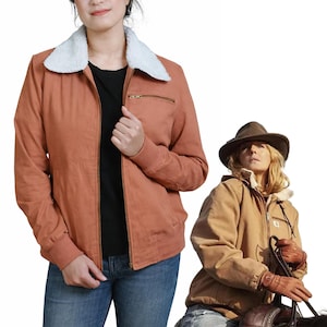 May include: A rust-colored jacket with a white faux-fur collar. The jacket has a zipper closure, a chest pocket, and ribbed cuffs. The model is wearing blue jeans and a black shirt. Another person is wearing a similar jacket in a tan color.