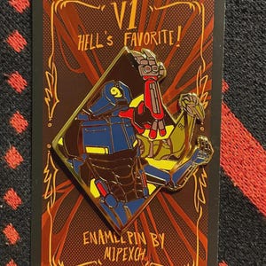 May include: Enamel pin featuring two robot figures in a diamond shape, with the text "V1 Hell's Favorite!" and "Enamel Pin by Mipexch". The pin has gold, blue, red, yellow, and brown colors.