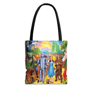 Może przedstawiać: Torba typu tote z czarnym uchwytem, przedstawiająca kolorową ilustrację postaci z Czarnoksiężnika z Krainy Oz. Obrazek przedstawia Dorotkę, Blaszanego Drwala, Stracha na Wróble i Tchórzliwego Lwa na żółtej ceglanej drodze.