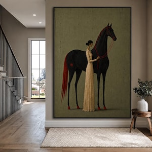 Puede incluir: Una impresión de arte mural enmarcada que muestra una figura alta y esbelta con un vestido beige hasta el suelo, de pie junto a un gran caballo negro. El caballo tiene una cola larga roja, cascos rojos y riendas rojas finas. Fondo verde oliva.