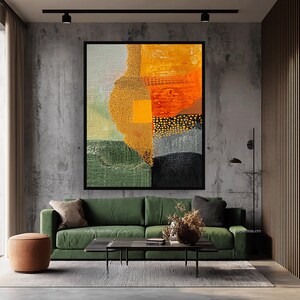 May include: An abstract painting in a black frame, featuring a mix of textures and colors. The artwork includes sections of green, yellow, orange, gray, and black. The painting hangs above a green sofa with a brown ottoman and a black coffee table.