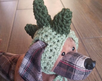 May include: A brown and tan plush dog wearing a green crocheted hat with a pointed top. The hat has a green and white plaid bow tie.