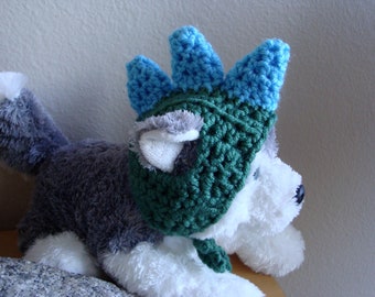 May include: A plush husky dog wearing a handmade crochet hat. The hat is primarily green with blue accents on the top, resembling a crown. The dog has gray and white fur.