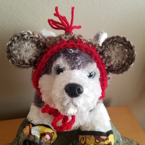 Könnte beinhalten: Ein Plüschhund, der eine rote und braune Häkelmütze mit Geweih trägt. Die Mütze hat einen roten Bommel oben drauf.