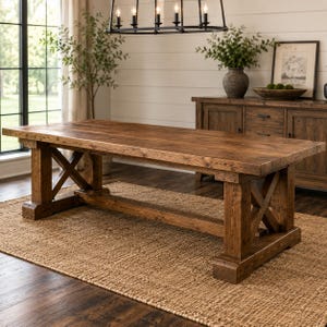 May include: A rectangular wooden dining table with a dark brown finish, featuring a thick tabletop and sturdy trestle legs connected by a central support beam. The base includes X-shaped cross-bracing on each end, providing a stable foundation.