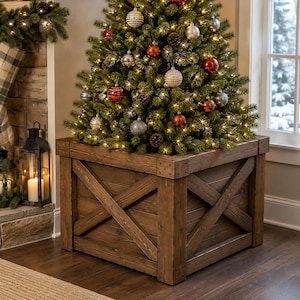 May include: A square wooden tree collar featuring a dark brown stained finish with a prominent X-brace design on each side. The base is constructed from horizontal planks with reinforced corner posts, housing a decorated Christmas tree with lights.