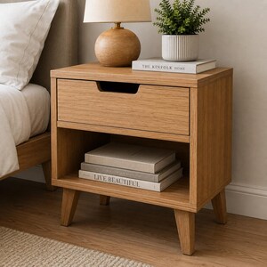 Peut inclure: Une table de chevet en bois de chêne clair dotée d'un tiroir unique avec une poignée encastrée et une étagère inférieure ouverte. Le dessus accueille une lampe ronde et une plante, tandis que l'étagère contient deux livres empilés.