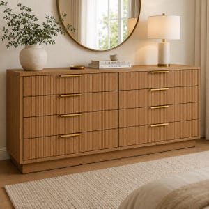 May include: A light brown wooden chest of drawers featuring eight drawers with vertical fluted detailing and slim horizontal gold metal handles. The chest of drawers has a rectangular frame and sits on a solid base, providing a clean and structured appearance.