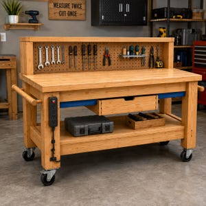 Op de afbeelding: Een werkbank van lichtgekleurd hout op wielen met een geperforeerd achterpaneel met diverse handgereedschappen, een centrale lade, een onderste opbergplank en een zwarte stekkerdoos aan de zijkant. De werkbank heeft een stevig frame en zwenkwielen.