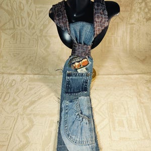 May include: A unique denim tie with a brown and blue patterned neckband. The tie is constructed from repurposed denim, featuring pockets and a patch that reads "High Sierra". The tie is displayed on a black mannequin head.