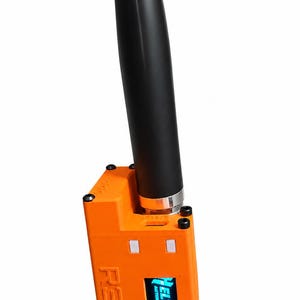 Puede incluir: Un dispositivo electrónico rectangular de color naranja brillante con una antena cilíndrica negra alta en la parte superior. El dispositivo presenta el texto R3.V en relieve en el lateral y una pequeña pantalla digital con el logotipo azul de Heltec Automation.