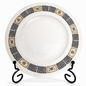 Peut inclure: Assiette en céramique blanche avec une bordure géométrique noire, dorée et blanche. L'assiette est présentée sur un présentoir en métal noir. La bordure présente un motif de clé grecque et des motifs circulaires. Un article décoratif pour la maison.