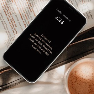 May include: A smartphone displays the text "James 4:7: Submit yourselves, then, to God. Resist the devil, and he will flee from you." The phone rests on a Bible, with a cup of coffee nearby.