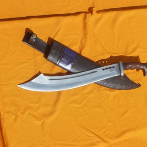 May include: A large, silver-bladed machete with a brown handle rests in a black sheath with purple accents. The blade has a curved edge and is set against a bright orange background.