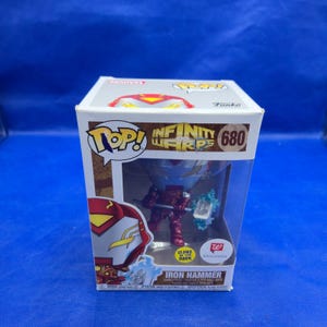 May include: A Funko Pop vinyl figure of Iron Hammer, number 680 from the Infinity Warps series, encased in its original cardboard box. The box features a clear plastic window, the character name, and a sticker indicating it glows in the dark.