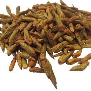 Może przedstawiać: Stos suszonych, wydłużonych pąków o mieszance zielonych i brązowych odcieni. Pąki mają teksturowany wygląd i są ułożone w gęstą grupę na białym tle. Obraz przedstawia produkt naturalny.