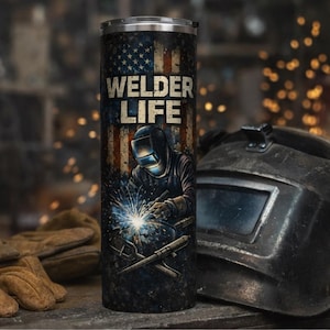Puede incluir: Un vaso de acero inoxidable con un diseño patriótico que presenta la bandera estadounidense y las palabras "WELDER LIFE". El vaso muestra a un soldador en el trabajo, junto con un casco de soldadura y guantes de trabajo.