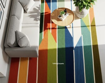 May include: A colorful area rug with a geometric design featuring vertical stripes and triangular shapes in shades of red, orange, yellow, green, blue, and white. A gray sofa, a round wooden coffee table, and a potted plant are also visible.