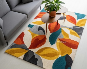 May include: A rectangular area rug with a cream background and a colorful leaf design. The leaves are in shades of orange, yellow, teal, gray, and red. The rug is placed in a living room setting with a gray sofa and two small wooden tables.