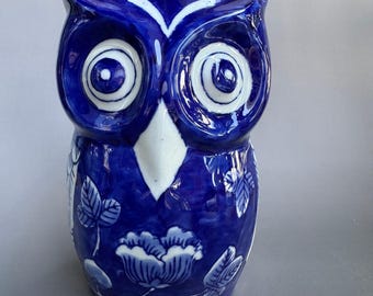 May include: A ceramic owl figurine featuring a deep blue and white color scheme. The owl has large, circular eyes, a pointed beak, and a body decorated with white floral and leaf patterns against a glossy, dark blue glazed surface.