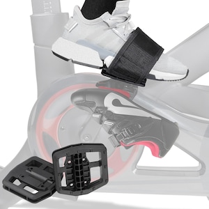 May include: Black exercise bike pedal straps securing a gray athletic shoe. The image also shows a pair of black exercise bike pedals and a partially visible exercise bike. The pedals are designed for use with athletic shoes.