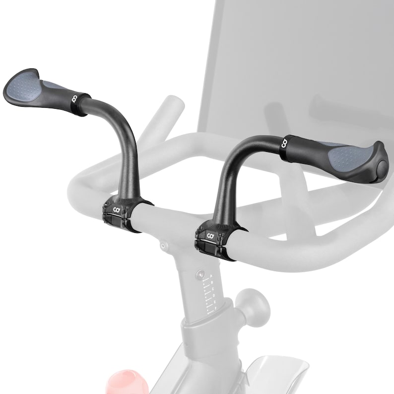 May include: Black exercise bike handlebars with gray padded grips. The handlebars are curved and attach to the bike frame with a clamp. The grips have a textured surface for a secure hold. The bike is shown in a studio setting.