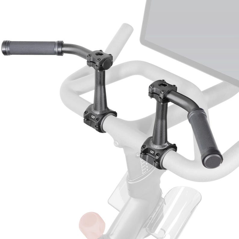 May include: Black bicycle handlebars with textured grips and a curved design. The handlebars are attached to the bike frame with black clamps. The image shows a close-up of the handlebars and the bike's frame.