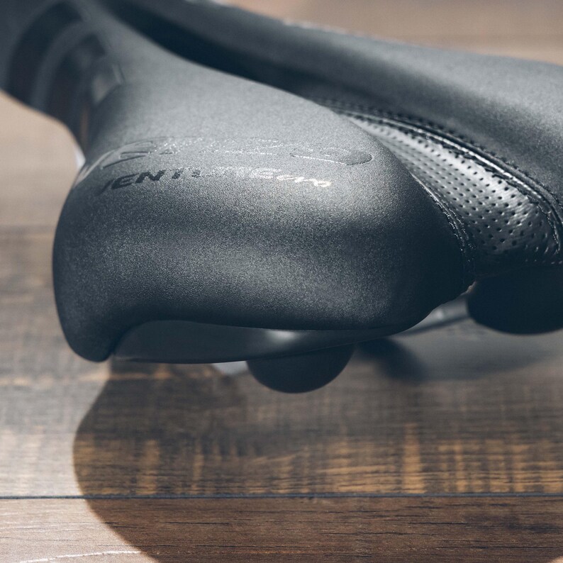 May include: Close-up of a black bicycle seat with the text "VENT" and "Zero" visible. The seat has a textured surface and a perforated leather section. The seat is designed for comfort and performance.