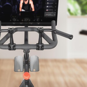 May include: Indoor stationary exercise bike with a digital display showing a workout in progress. The bike has a dark gray frame, padded handlebars, and a red adjustment knob. The screen displays workout metrics.