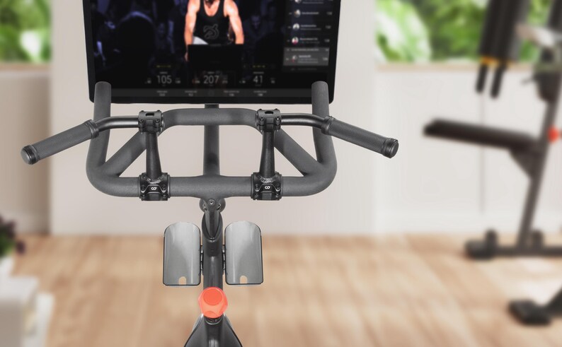 May include: Indoor stationary exercise bike with a digital display showing a workout in progress. The bike has a dark gray frame, padded handlebars, and a red adjustment knob. The screen displays workout metrics.