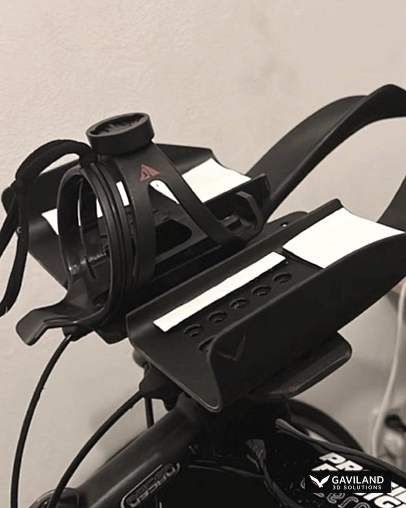 May include: Black bicycle handlebar with a water bottle cage and a computer mount. The handlebar has white accents and is attached to a black bicycle frame. The image is a close-up shot.