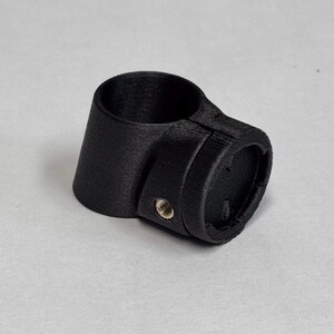 May include: A matte black 3D printed cylindrical mounting bracket featuring a circular opening and a side-mounted metal threaded insert. The component has a textured surface finish and includes the text GAVILAND 3D SOLUTIONS in the corner.