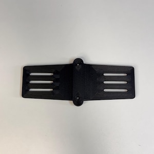 May include: A black, rectangular component featuring three horizontal slots on each side. It has two circular holes at the top. This part is likely a component of a larger item.