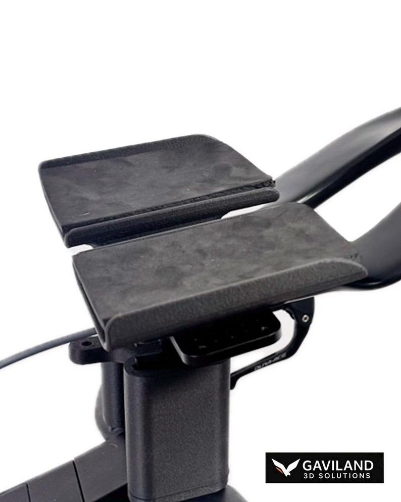 Puede incluir: Un conjunto de acoples de triatl&oacute;n para bicicleta en color negro con dos apoyabrazos texturizados sobre una estructura central. Incluye una peque&ntilde;a palanca negra con la etiqueta Dura-Ace y un logo en la esquina inferior Gaviland 3D Solutions.