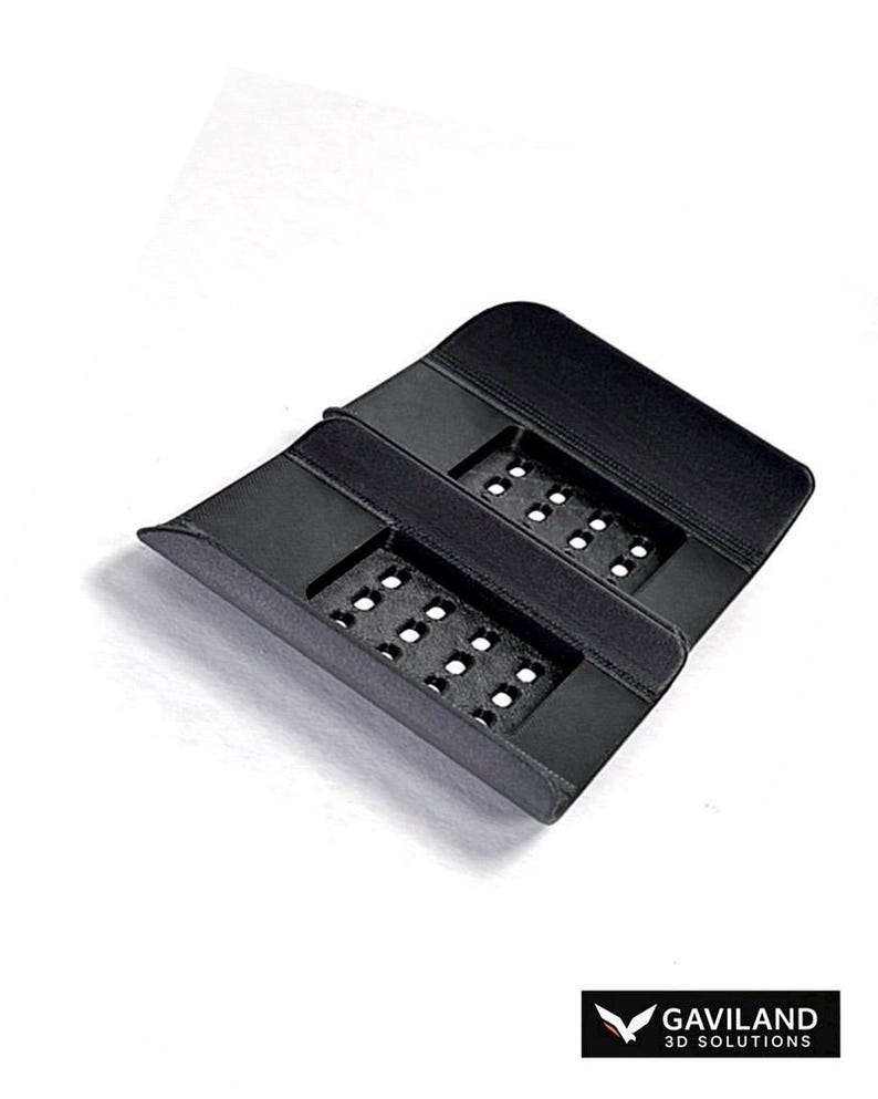 Puede incluir: Un soporte negro rectangular de pl&aacute;stico impreso en 3D que presenta dos secciones empotradas y perforadas con m&uacute;ltiples peque&ntilde;os agujeros cuadrados. El objeto tiene un acabado mate liso e incluye el texto GAVILAND 3D SOLUTIONS en la esquina.