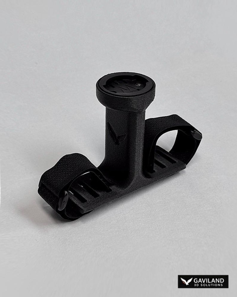 May include: A black bicycle computer mount with a circular top and a strap for securing to handlebars. The mount has a textured surface and a logo on the front. The Gaviland 3D Solutions logo is in the bottom right corner.