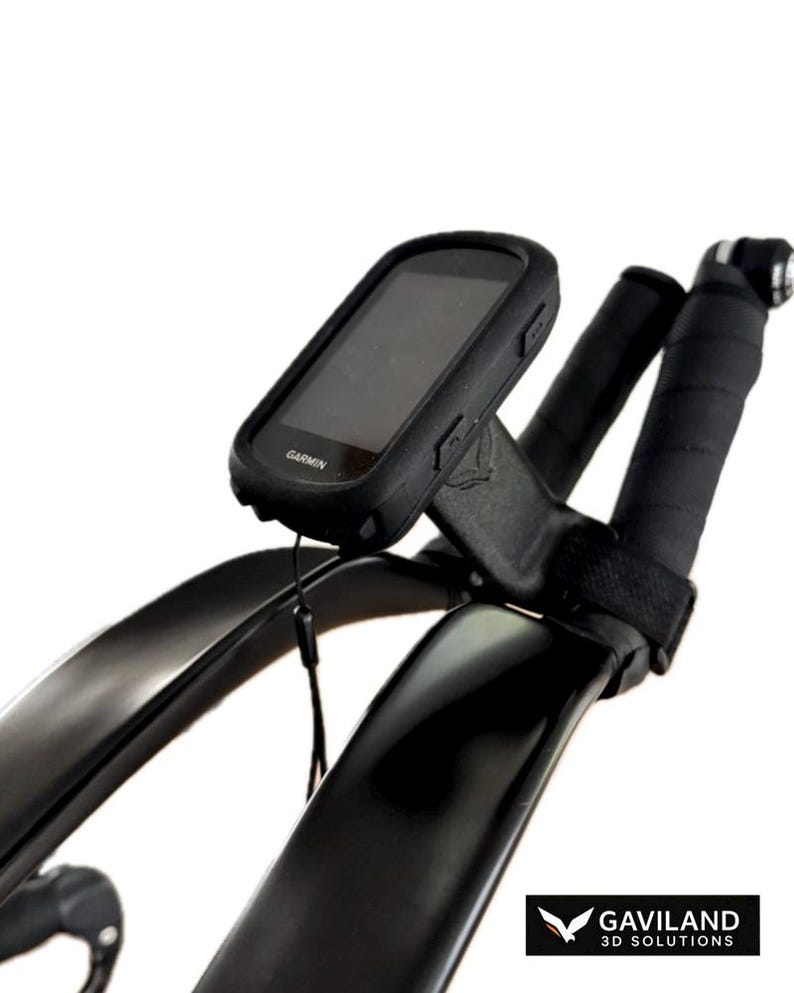 May include: Black Garmin cycling computer mounted on black bicycle handlebars. The computer is in a black protective case. The handlebars are wrapped in black tape. The image is set against a white background.