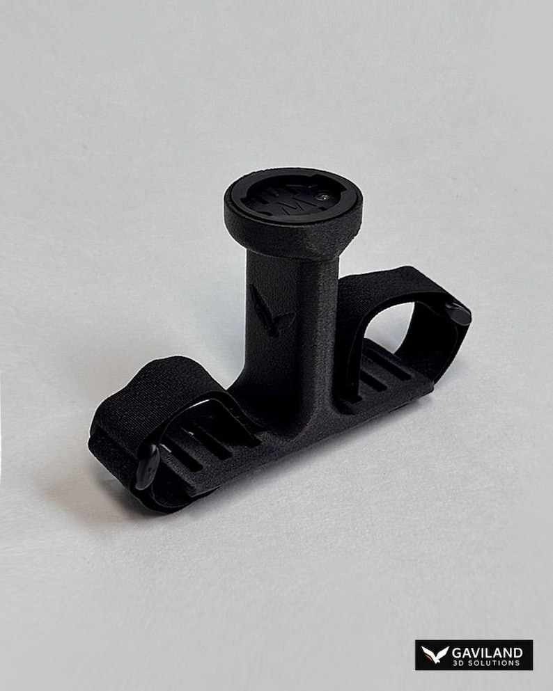 May include: A black bicycle computer mount with a circular top and a strap for securing to handlebars. The mount is designed to hold a cycling computer and is made of a textured material. The Gaviland 3D Solutions logo is in the bottom right corner.