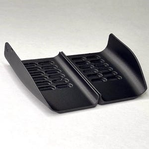 May include: A black, two-piece plastic component featuring a curved, ramp-like design with a series of elongated, oval-shaped ventilation slots on each section. The object is matte in texture and includes the text GAVILAND 3D SOLUTIONS in the corner.