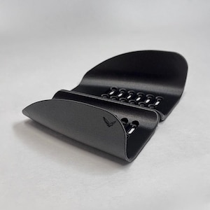 May include: A matte black, curved plastic phone stand featuring a series of ventilation slots along the base and a small bird logo embossed on the front. The bottom right corner displays the text GAVILAND 3D SOLUTIONS with a bird icon.