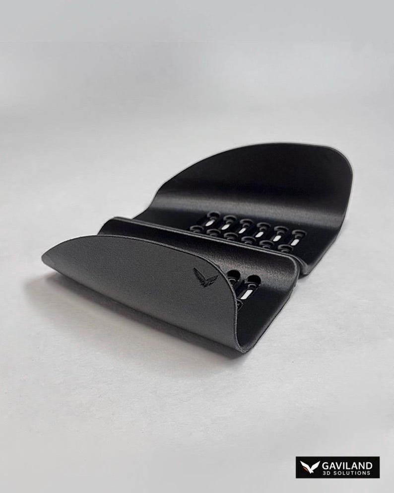 May include: A matte black, curved plastic phone stand featuring a series of ventilation slots along the base and a small bird logo embossed on the front. The bottom right corner displays the text GAVILAND 3D SOLUTIONS with a bird icon.