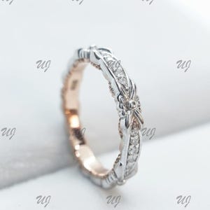 Puede incluir: Un anillo de plata y oro rosa con un diseño delicado. El anillo presenta una banda con pequeñas piedras brillantes y detalles intrincados. El diseño del anillo incluye un elemento en forma de lazo. El anillo es una joya.