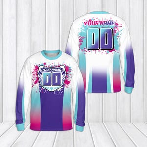 May include: A long-sleeved jersey featuring a white base with purple, teal, and pink paint splatter patterns. The front displays a shield graphic with the text YOUR NAME and 00, while the back shows the text YOUR NAME and 00 in large font.