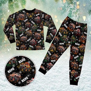 May include: A black long-sleeve pajama set featuring a repeating pattern of monster trucks, snowflakes, and the word NAME printed in white. The set includes a crew-neck top and matching pants, with some trucks wearing Santa hats.