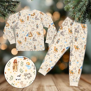 Puede incluir: Un conjunto de camisa de manga larga y pantalones en color crema con un estampado repetitivo de escena de natividad con camellos, ovejas, ángeles y figuras. El texto "Holy Night" y "Glory to God" se intercala entre hojas verdes y estrellas amarillas.