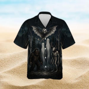 May include: A black short-sleeve button-down shirt featuring a dark forest scene with a large bat with a skull head, two tall ghostly figures, a hairy ape-like creature, and a skeletal deer-like figure with antlers in a monochromatic style.
