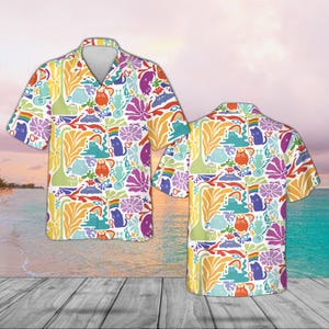 May include: A short-sleeved button-down shirt featuring a vibrant, colorful pattern of cats, rainbows, and floral designs. The shirt has a white background with a V-neck collar and is displayed with its back view.